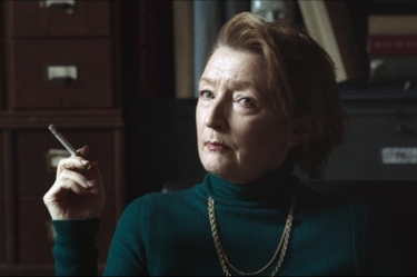 A film still from 'Winter of the Crow'. The images shows Lesley Manvilles character looking past the camera and holding a cigarette.