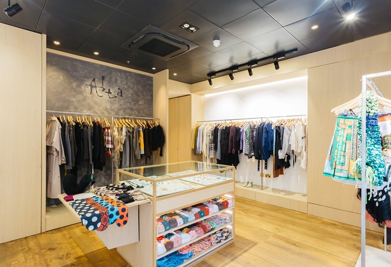 Inside Alta Store. A display unit in the middle, jewellery encased in glass on the top and clothes folded underneath. Around the walls there are various clothes hanging on three railings.