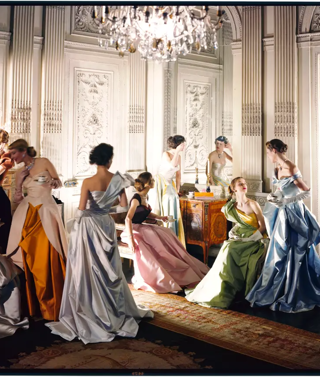 A group of women in coloured evening dresses pose in ballroom