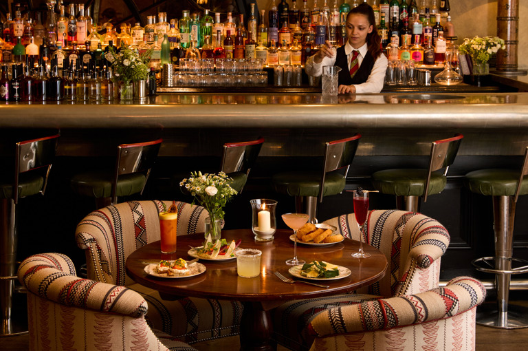 An image to promote Brasserie Max’s À La Carte menu at Covent Garden Hotel. The image shows a variety of dishes on the round table and a selection of cocktails.