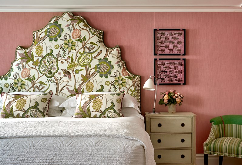 Front bedroom shot the bed in a deluxe room, 005, at Knightsbridge Hotel with plain light pink walls and green nature drawings on the headboard and pillows.