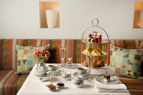 The Kit Kemp Design Stories Afternoon Tea set up at The Whitby Bar. There is a cake stand with scones, cakes decorated with Kit Kemps Famous fabrics, edible mannequins and sandwiches with tea and Champagne