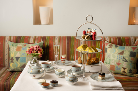 The Kit Kemp Design Stories Afternoon Tea set up at The Whitby Bar. There is a cake stand with scones, cakes decorated with Kit Kemps Famous fabrics, edible mannequins and sandwiches with tea and Champagne