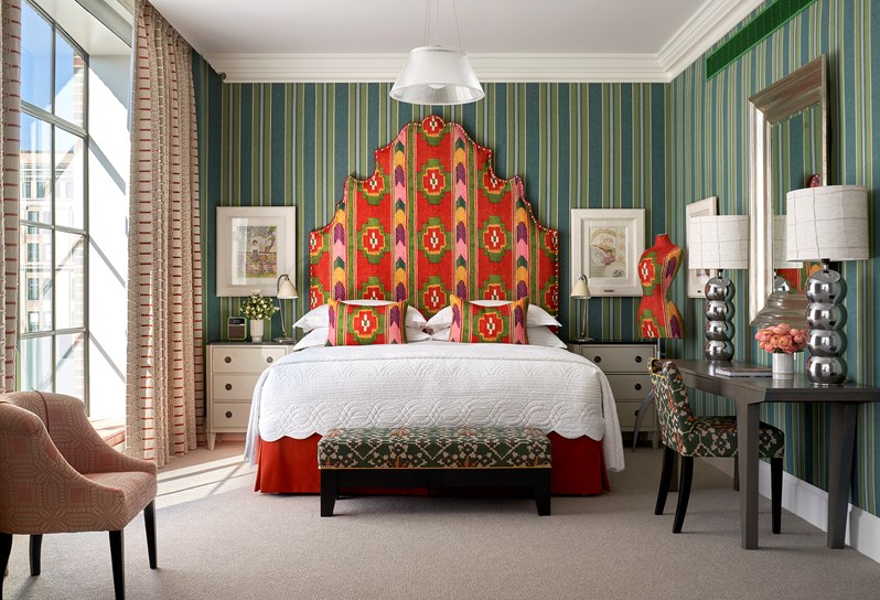 Shot of the bedroom in a One Bedroom Suite at the Crosby Street Hotel with a large bed, red patterned oversized headboard and nuances of green striped walls