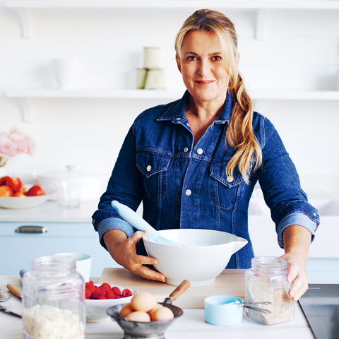 Chef Donna Hay holding baking equipment in a kitchen. She has a large bowl and is surrounded by ingredients