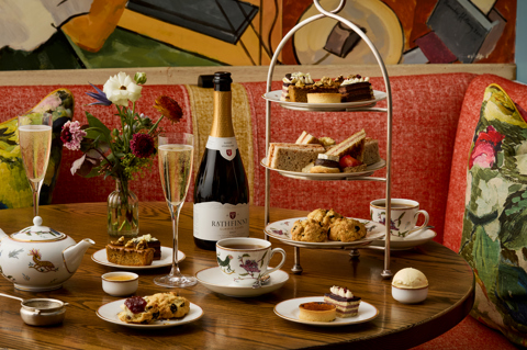 A wide shot of the Bloomsbury Set Afternoon Tea at Oscar: There is one afternoon tea stand on the table next to a bottle of sparkling wine