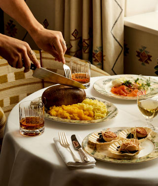 Portrait shot of a table set for Burns Night dinner with Bruichladdich at Covent Garden Hotel. There is a plate of haggis being cut open, plates of scallops and smoked salmon and glasses of whisky.