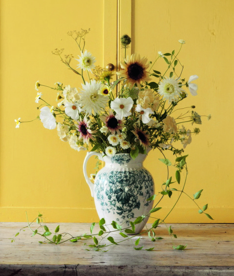A image from Harriet Thistlethwayte's new book 'A Country Style'. The image shows a gorgeous arrangement of flowers from Harriet's garden in a vase with a bright yellow backdrop. 