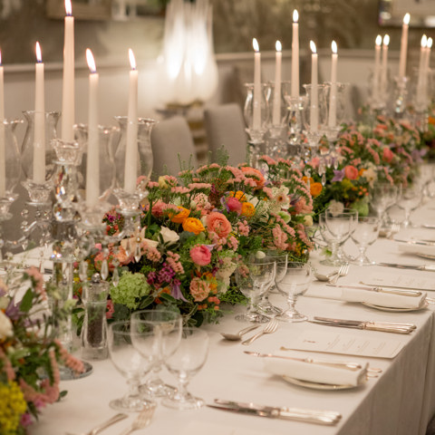 Close up portrait shot of a long dining table dressed with colourful flowers and tall candlesticks in the Shooting Gallery private events room at Haymarket Hotel
