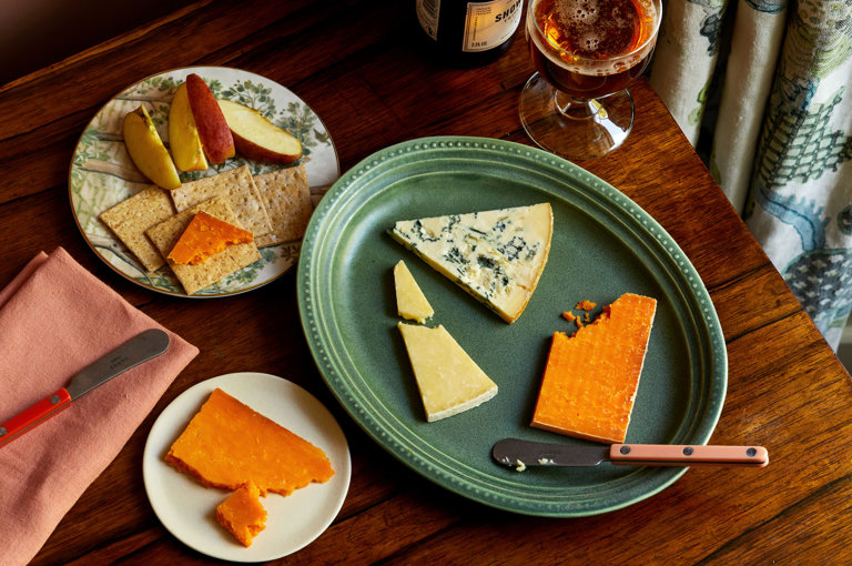 An image of a table with multiple different plates with cheeses and a glass of beer at The Potting Shed, Dorset Square Hotel. 