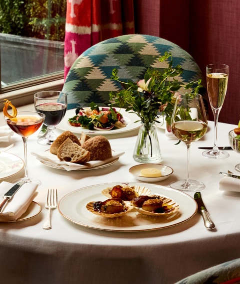 A table in front of a window at Brumus laid with four appetisers accompanied by glasses of wine and cocktails