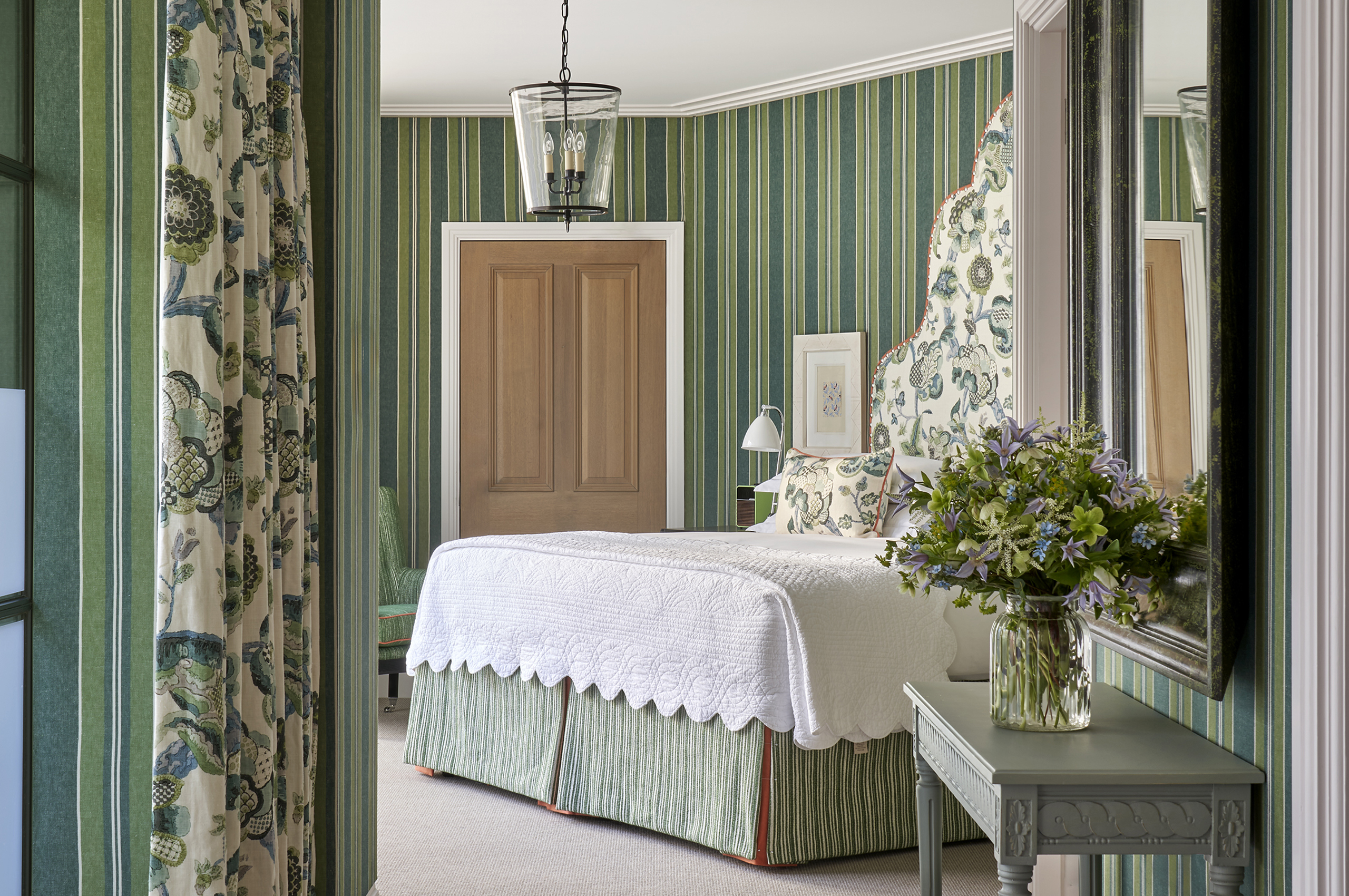 Bedroom with striped wallpaper, white bed, and floral vase