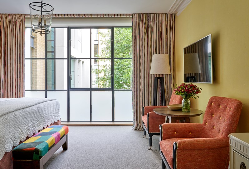 A bedroom at Ham Yard Hotel with floor-to-ceiling crittal-style windows and two orange chairs with yellow buttons