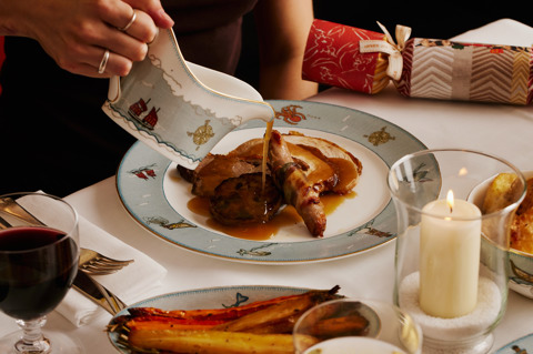 This image shows a close up image of the Turkey main dish, with roast vegetables in the foreground on Sailors Fairwell crockery . You can see someone pouring gravy over their plate of food. This is to promote the Christmas Day Menu at Ham Yard Hotel.