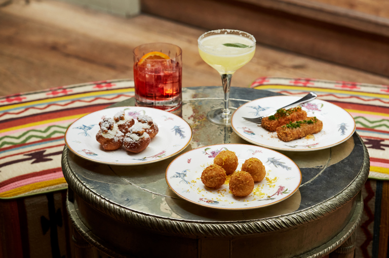 Wide shot of bar food on a table at The Potting Shed. Plates of arancini and croquettes with two cocktails