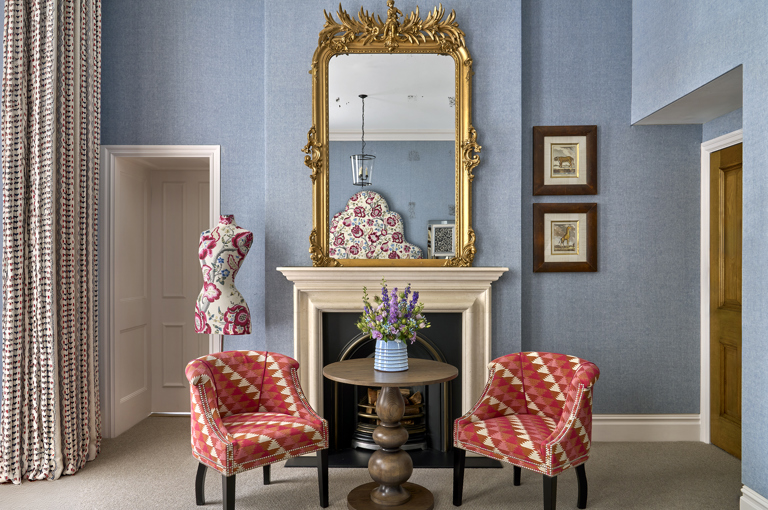 A wide shot of the sitting area in Junior Suite 102 at Knightsbridge Hotel, featuring two arm chairs and a round table in front of a fireplace