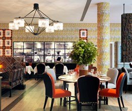 Tables beautifully set for dining in the quirky and playfully decorated restaurant, looking in toward the open plan kitchen with large windows, seeing three chefs at work.