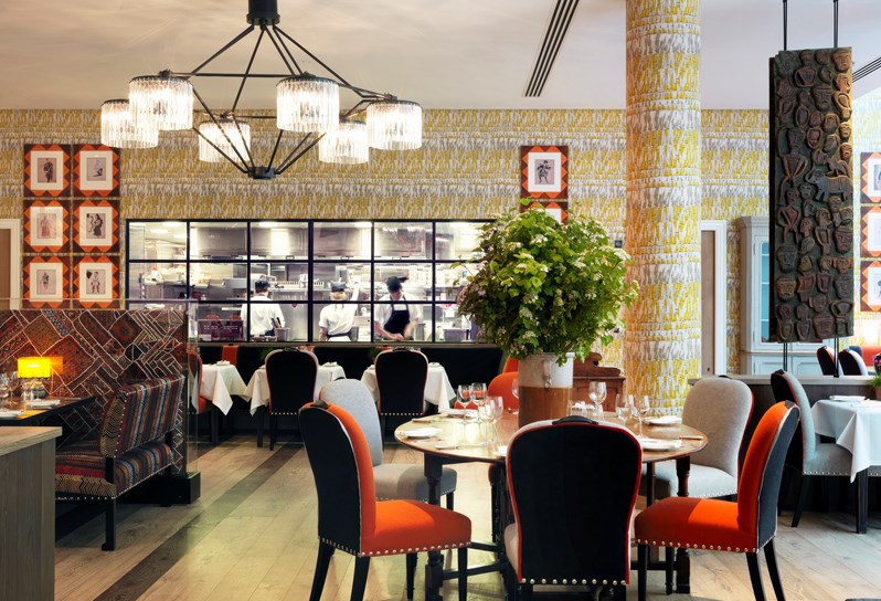Tables beautifully set for dining in the quirky and playfully decorated restaurant, looking in toward the open plan kitchen with large windows, seeing three chefs at work.