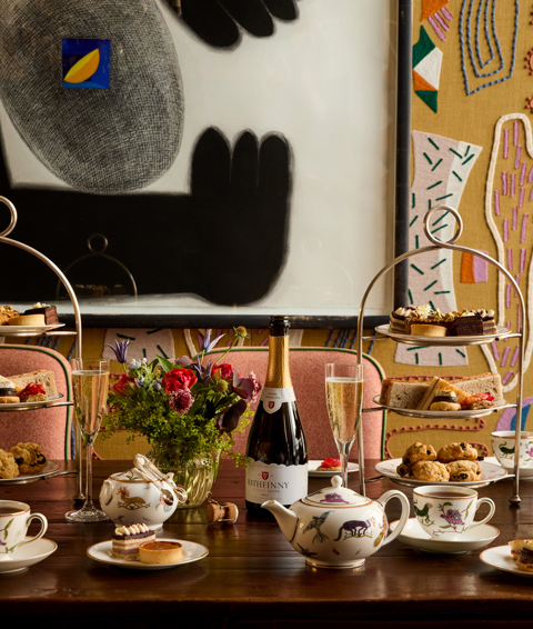 A portrait shot of the Afternoon Tea in the Dora Carrington Room at Charlotte Street Hotel: There are two afternoon tea stands on the table being served with a bottle of sparkling wine
