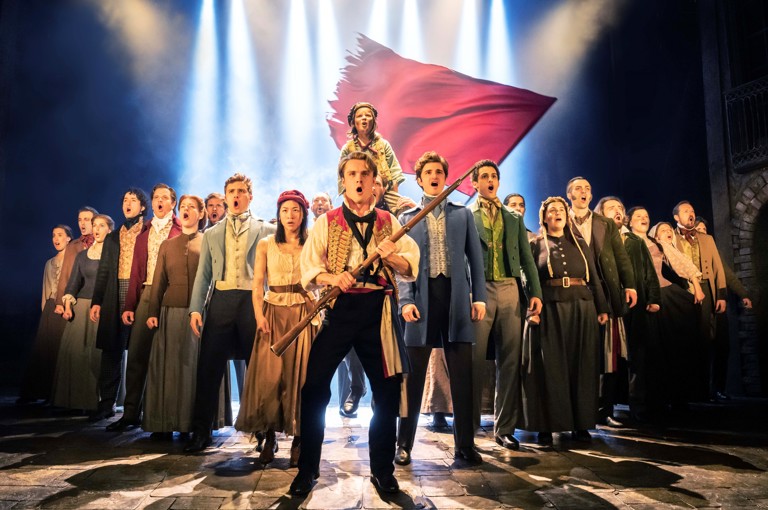 The ensemble cast of Les Miserable singing on stage