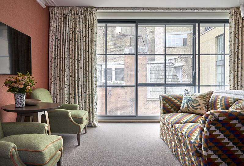A room at Ham Yard Hotel with floor-to-ceiling crittal-style windows, a sofa and two chairs