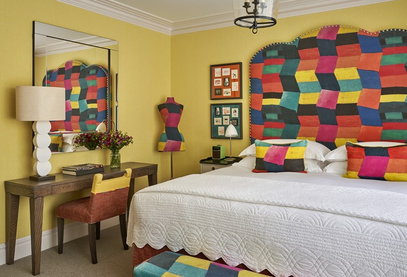 A bedroom at Ham Yard Hotel with a multicoloured statement headboard and dressing table and chair