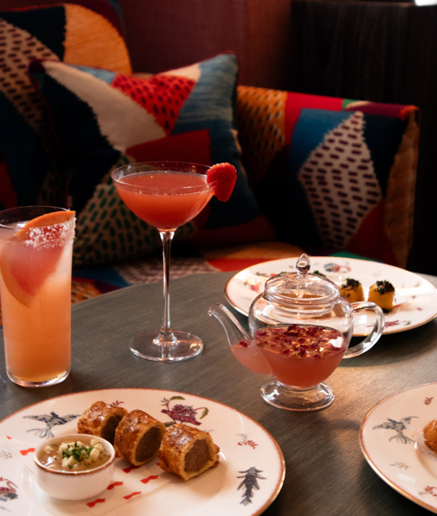Three pink coloured cocktail and plates of bar snacks at Haymarket Hotel