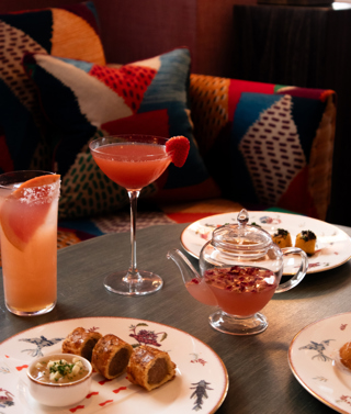 Three pink coloured cocktail and plates of bar snacks at Haymarket Hotel