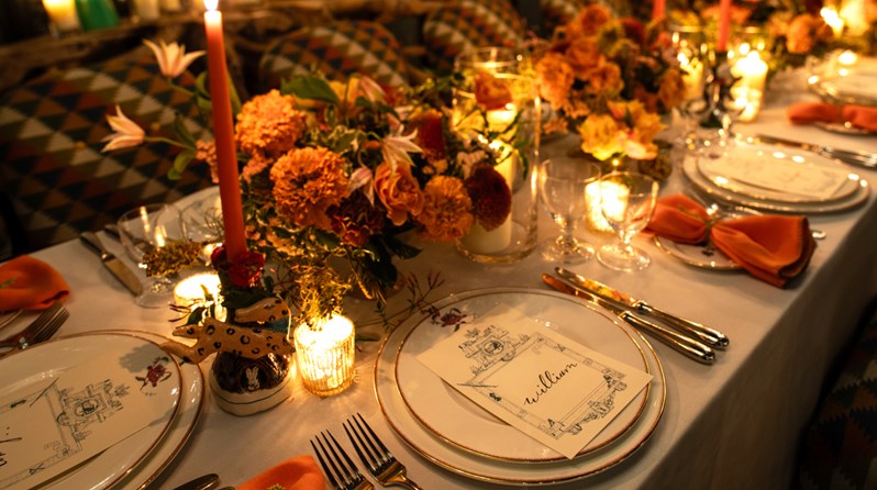 A close up image of a long table set up for dinner with dim candle lighting in The Orangery at Crosby Street Hotel.