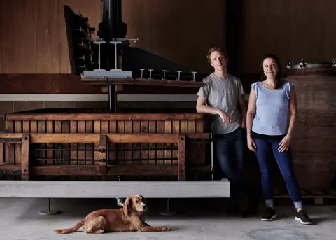 A wide angle shot of two of the owners and their dog inside the winery at Offbeat Wines